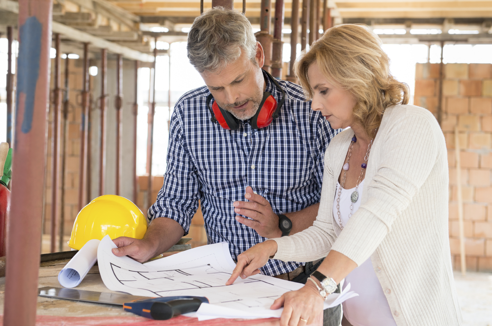 Portrait Of Male Architect And Mature Woman Discussing Plan On Blueprint At Construction Site